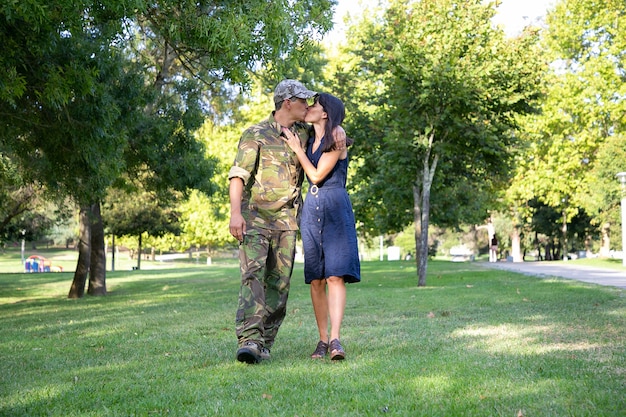 公園の芝生の上で抱き合ったり キスしたり 一緒に歩いたりする愛情のある白人カップル 軍服を着た中年の兵士が かわいい妻を抱きしめています 家族の再会 週末 帰国のコンセプト 無料の写真