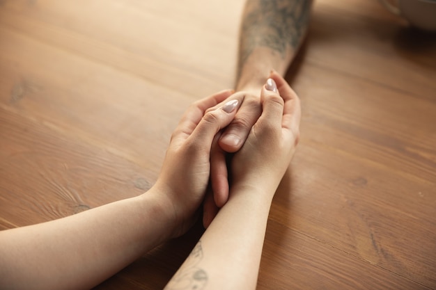 Loving couple holding hands close-up on wooden desk Free Photo