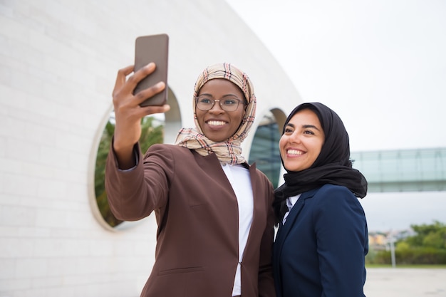 Low Angle Shot Of Smiling Muslim Businesswomen Taking Selfie