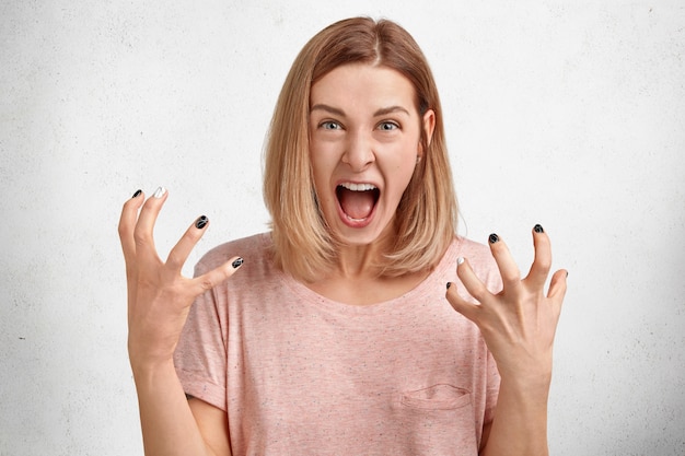 Mad irritated young woman screams loudly and gestures actively, being dissatisfied and annoyed with something, expresses her displeasure and annoyance Free Photo