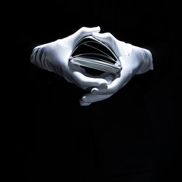 Magician's hand wearing white glove holding playing cards stack Free Photo