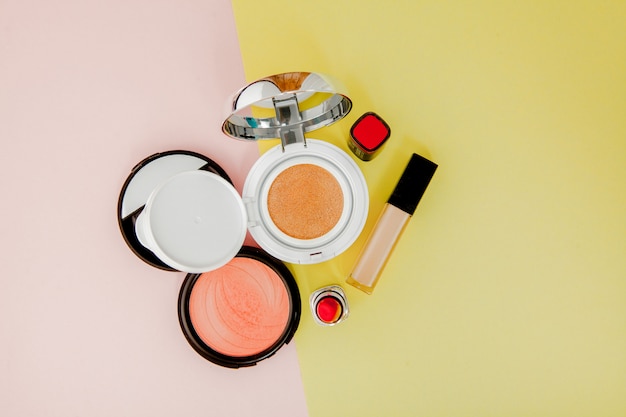 Make up products spilling on to a bright yellow and pink background with copy space Premium Photo
