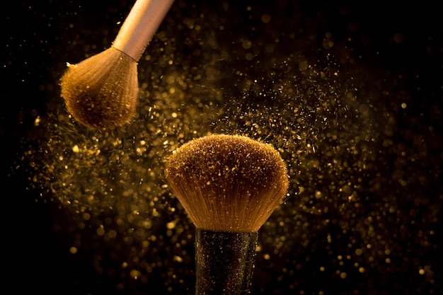 Makeup brush with golden cosmetic powder spreading on black background Premium Photo