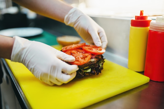 Premium Photo | Male cook puts tomatoes in to the burger, fast food ...