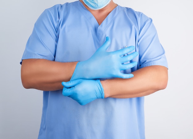 Male Doctor In Blue Uniform Puts On His Hands White Sterile Latex