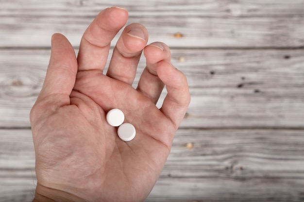 Male hand holding pills on wooden background Premium Photo