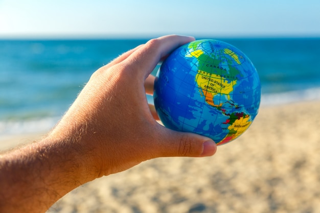 Premium Photo | Male hand holds globe of planet earth on a seaside ...