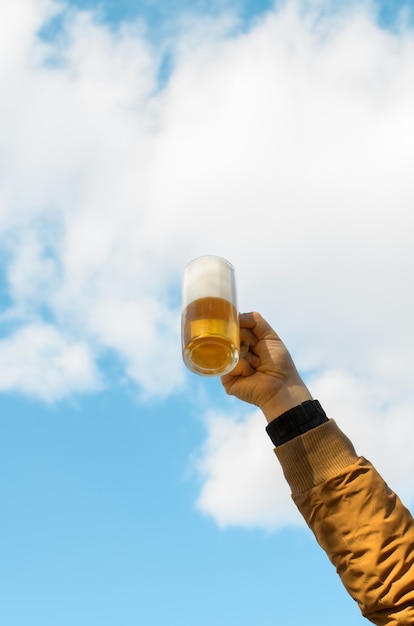 Premium Photo | Male hand raising a mug of beer in cheer against the ...