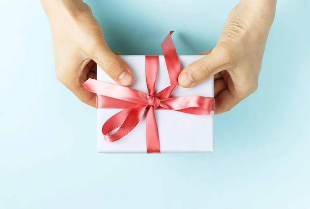 Male hands holding gift box with ribbon on blue background Premium Photo