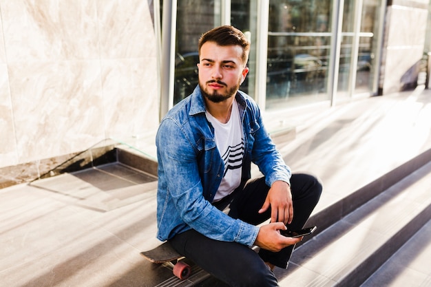 Free Photo | Male skateboarder sitting on skateboard with smartphone