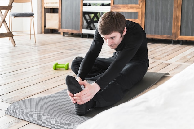 Free Photo | Male stretching legs on exercise mat