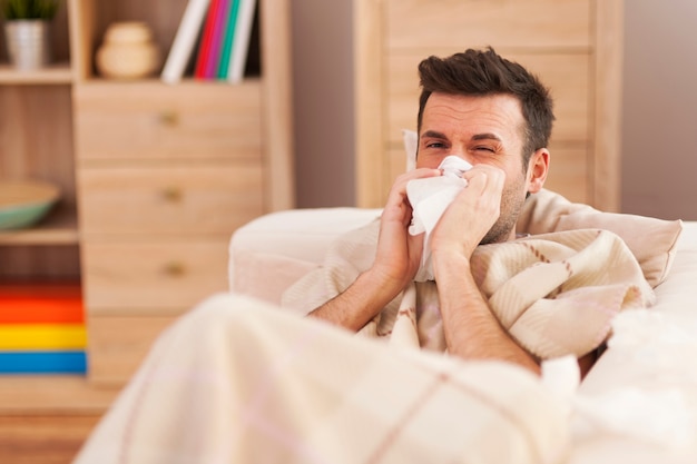 Man blowing his nose while lying sick in bed Free Photo