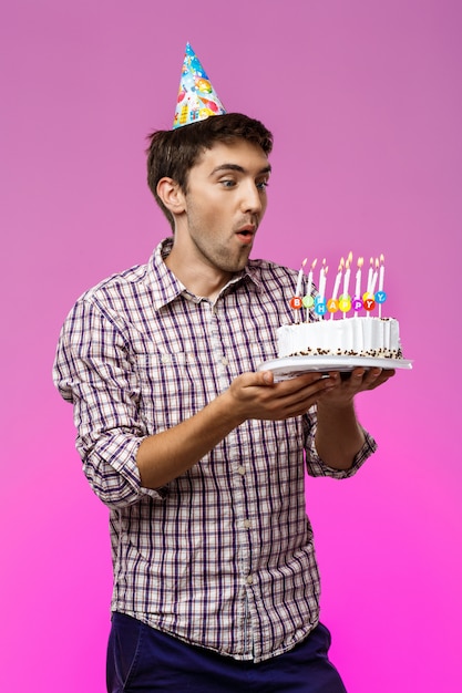 Free Photo Man Blowing Out Candles On Birthday Cake Over Purple Wall