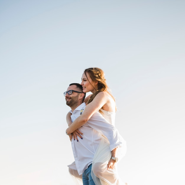 Man carrying his girlfriend on his back at a beach against blue sky Free Photo