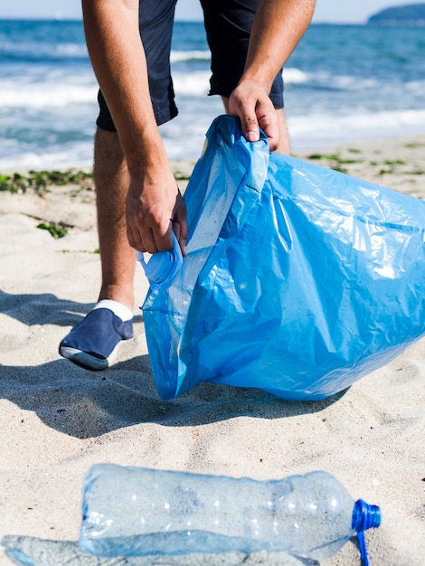 Man collecting plastic trash from the beach and putting it into blue garbage bags for recycle Free Photo