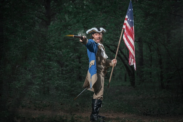 ピストルとフラグを持つアメリカのアメリカ独立戦争の兵士に扮した男 プレミアム写真