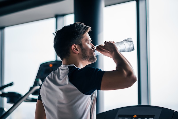 premium-photo-man-drinking-water-while-working-out-on-treadmill-in