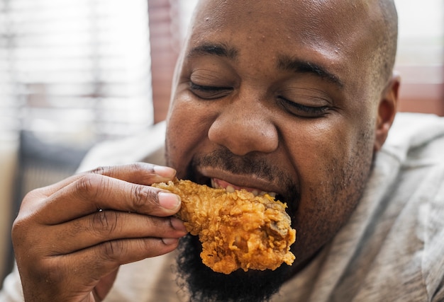 Man eating a piece of fried chicken Free Photo