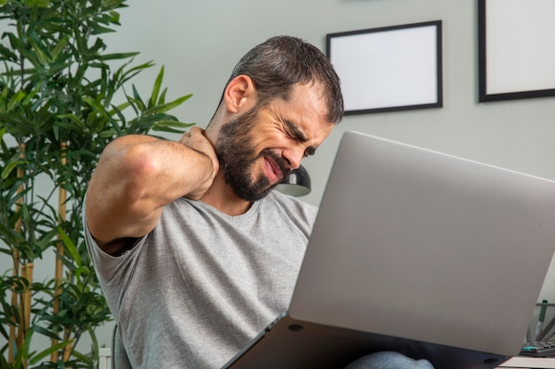 Man experiencing neck pain while working from home on laptop Free Photo