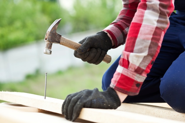 Premium Photo | Man hammering a nail in a plank on the roof