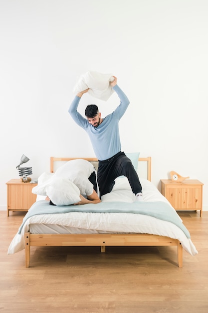 Free Photo | Man hitting his boyfriend with white pillow on bed