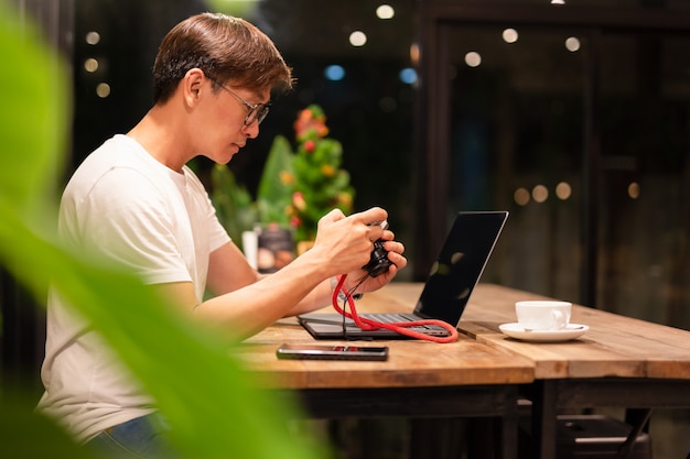 Man holding digital mirrorless camera checking photo with laptop on the table. Premium Photo