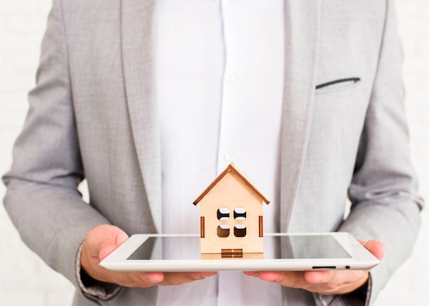 Man holding a wooden house on a tablet Free Photo