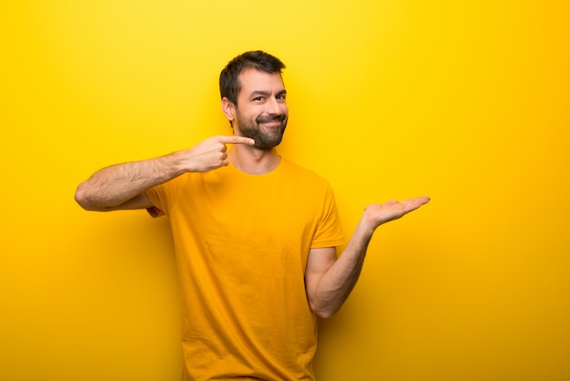 Man on isolated vibrant yellow color holding copyspace imaginary on the palm to insert an ad Premium Photo