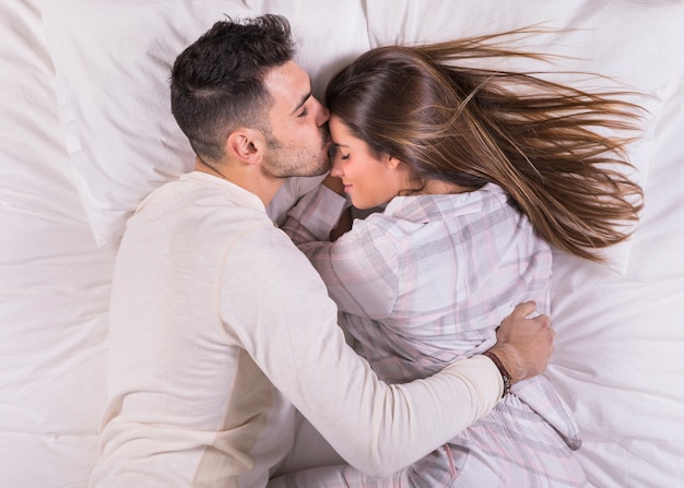 男がベッドの中でおでこに女性にキス 無料の写真