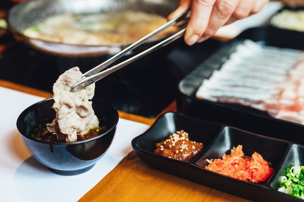 Man pinching boiled well done kurobuta pork and dipping in ponzu sauce with tong. Premium Photo