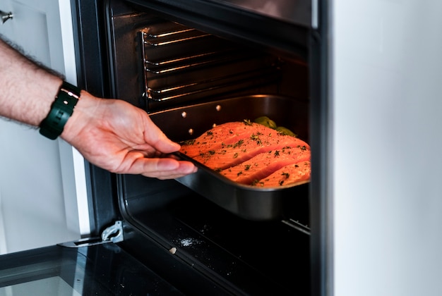 Free Photo | Man putting raw salmon steak into oven