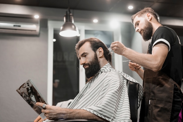 Man Reading Magazine While Cutting Hair In Barber Shop Free Photo