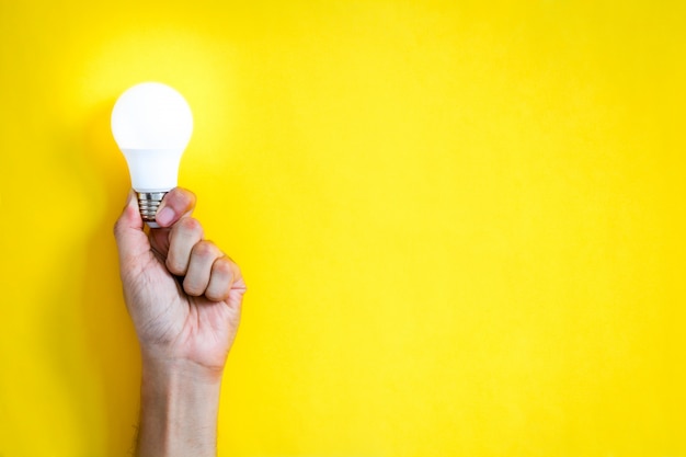 Premium Photo | Man's hand holding led light bulb over yellow color