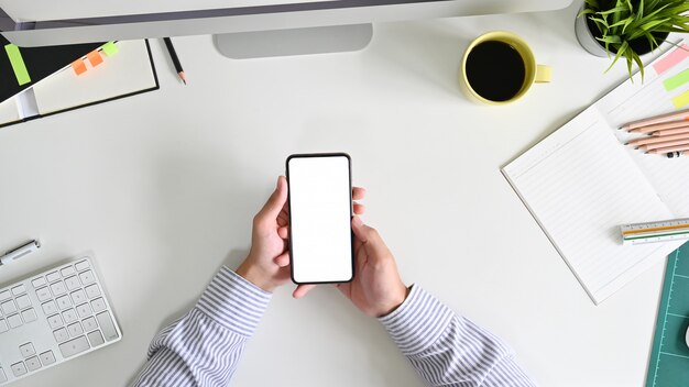 Man's hs holding smartphone empty screen on office desk with top view. Premium Photo