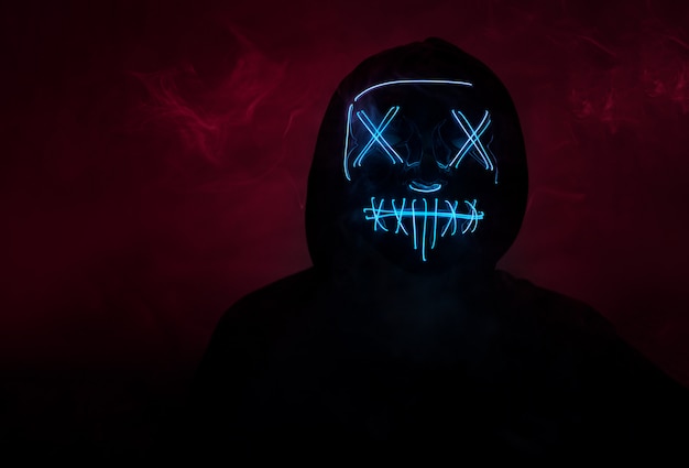 Premium Photo | A man in a scary neon glowing mask and a hood on a dark ...