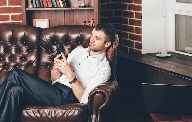 Premium Photo | A man sits on a comfortable leather sofa and holds the ...