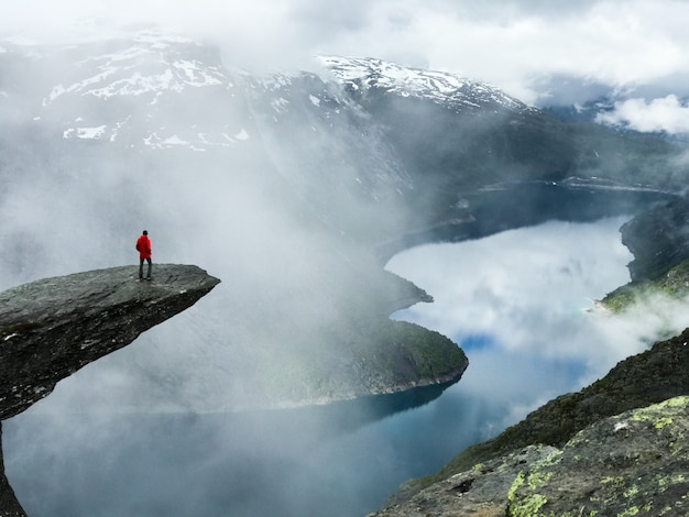 Man sits at the end of trolltunga before the mountains Free Photo