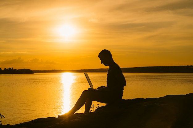 Premium Photo | A man sits on the river bank with a laptop in his hand ...