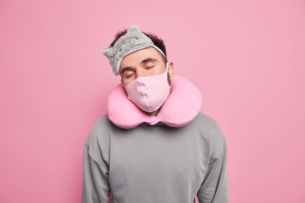 Man sleeps while traveling in transport during coronavirus outbreak wears sleepmask protective face mask and sleeping pillow has nap dressed in casual jumper Premium Photo