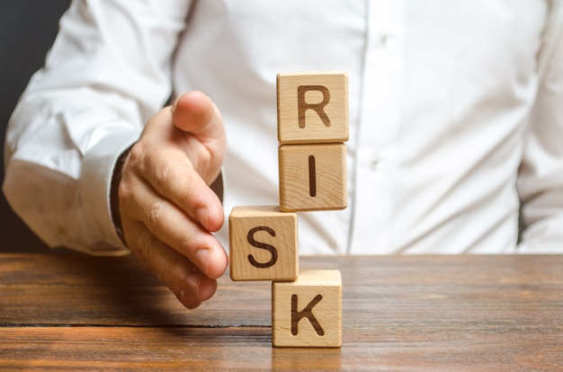 A man straightens a segment in an unstable tower of cubes labeled risk. risk management Premium Photo