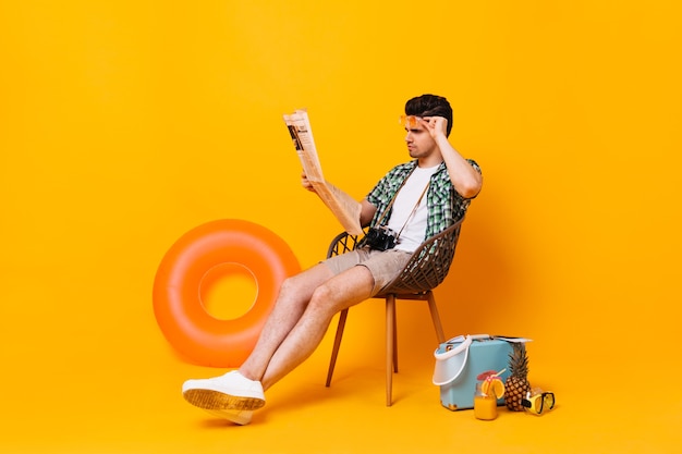 Free Photo Man In Summer Outfit Removes Glasses And Reads Newspaper Portrait Of Guy On Orange Space With Suitcase And Rubber Ring