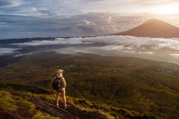 Man tourist looks at the sunrise on the volcano batur on the island of blai in indonesia. hiker man with backpack travel on top volcano, travel concept Premium Photo