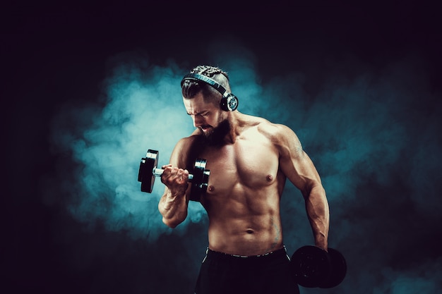 Premium Photo | Man training muscles with dumbbells in studio on dark ...