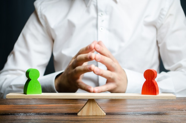 A man with hands in the lock and looks at the rival red and green figures on a scales Premium Photo