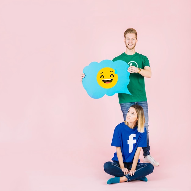 Man with laughing emoji speech bubble standing behind thoughtful woman Free Photo