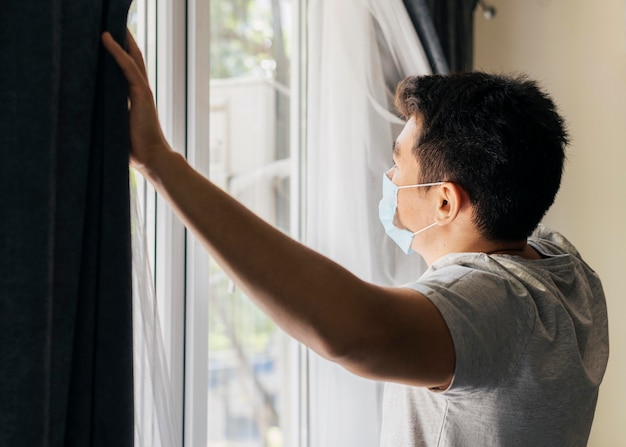 Man with medical mask at home during the pandemic opening the window curtains Free Photo