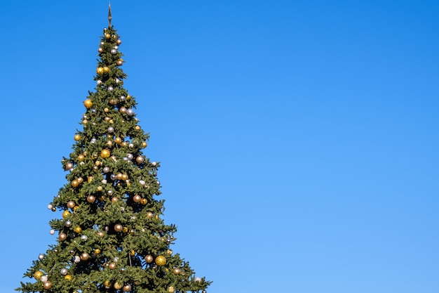 青い空に屋外の巨大な人工的なクリスマスツリーの多くの装飾と花輪 晴れた夏の日 プレミアム写真