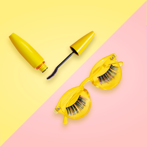 Mascara in yellow tube with open brush on pink and yellow sunglasses with fake eyelashes. Premium Ph