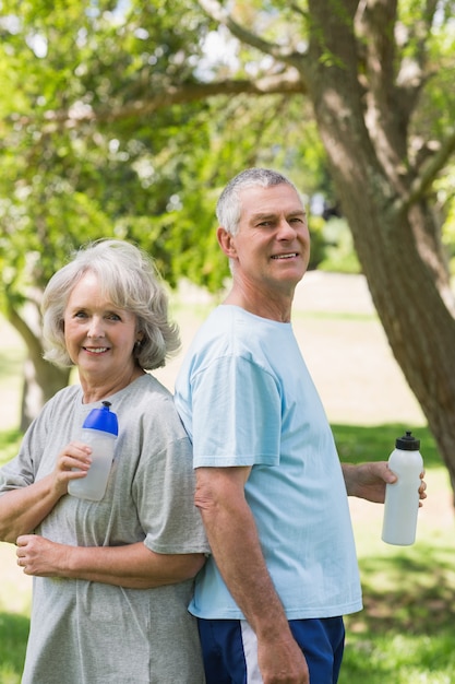 Premium Photo Mature Couple Standing With Water Bottles At Park