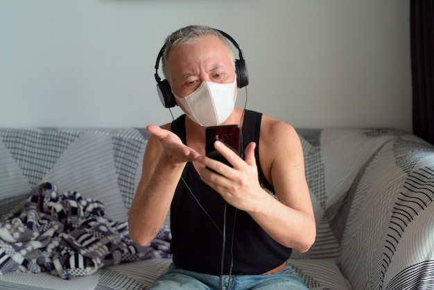 Premium Photo Mature Japanese Man With Mask Video Calling With Headphones At Home Under Quarantine